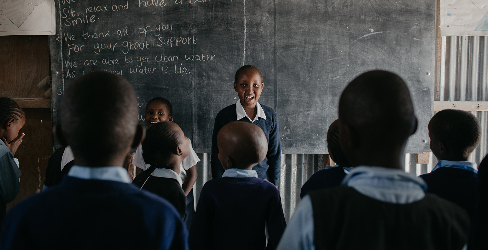 alt="Sienna_meets_Praise_in_Kenia_im_Kinderzentrum_lachende_Kinder_in_der_Schule_vor_einer_Tafel_Compassion_Afrika_Compassion_Deutschland"